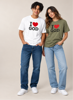 A man and a woman modeling matching graphic t-shirts with 'I [heart] GOD' printed on the front. The man wears a white t-shirt and blue jeans, while the woman wears an olive green t-shirt and light-wash blue jeans, standing against a solid beige studio background.